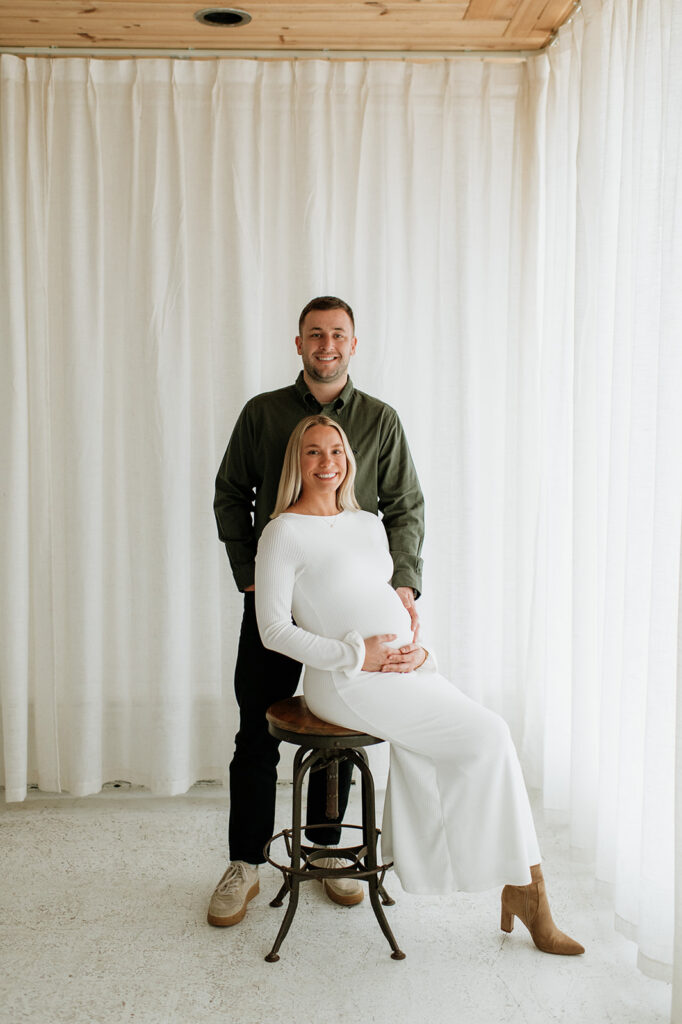 Pregnant woman seated on a stool with her partner standing behind her during South Bend Indiana maternity photos.