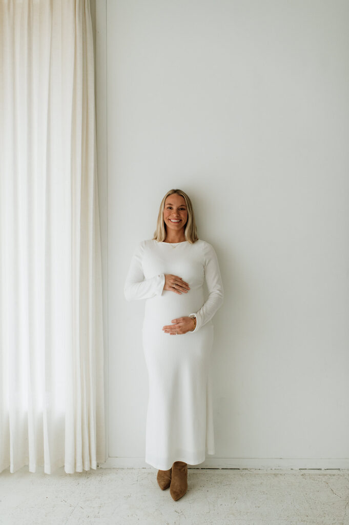 Pregnant woman smiling while holding her belly during her studio South Bend, Indiana maternity photos at Area Hall Art House.