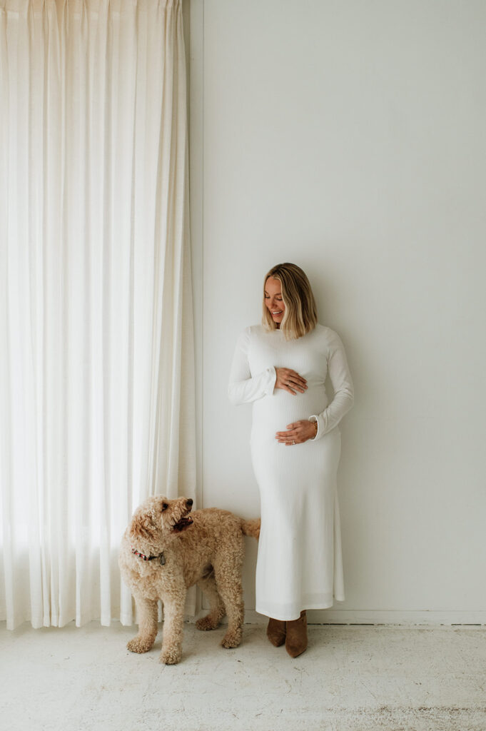 Pregnant woman standing near a window with her dog during studio South Bend Indiana maternity photos.