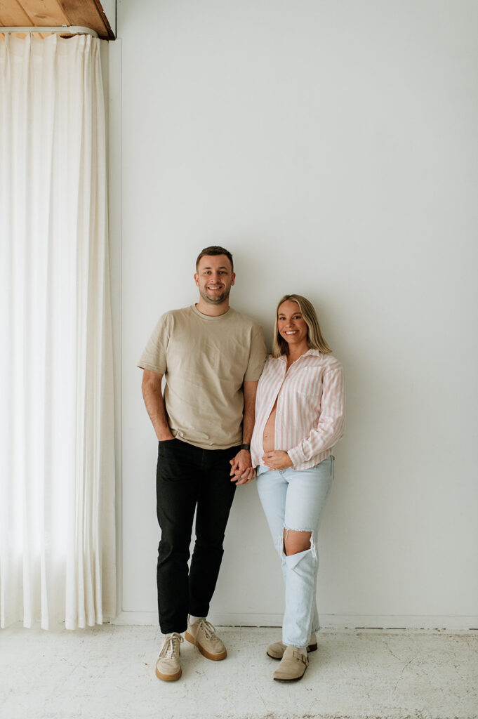 Expecting couple holding hands in casual outfits during a relaxed studio maternity session at Area Hall Art House in South Bend, Indiana.