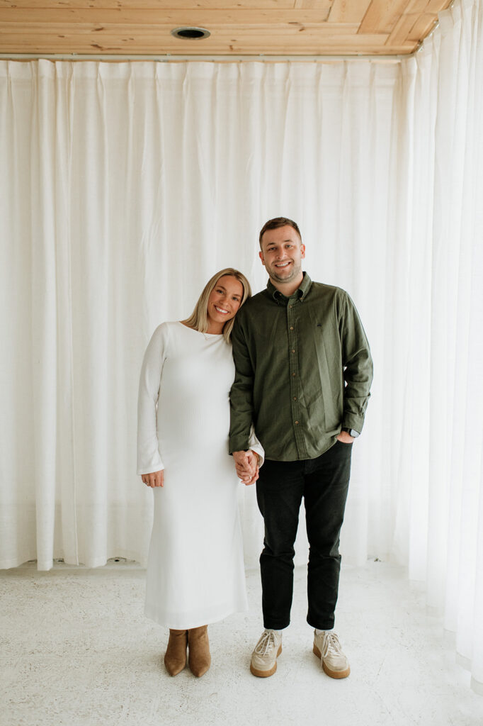 Couple standing together in front of white curtains during South Bend Indiana maternity photos at Area Hall Art House.