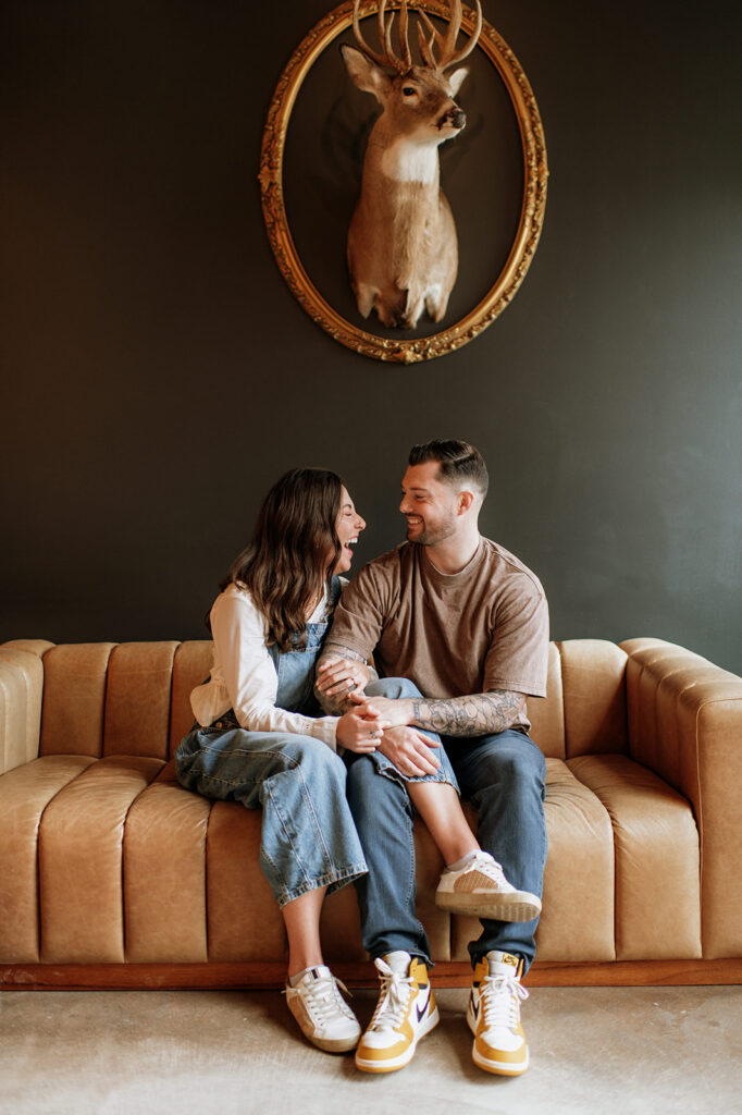 Couple laughing together on couch in antique shop engagement session.