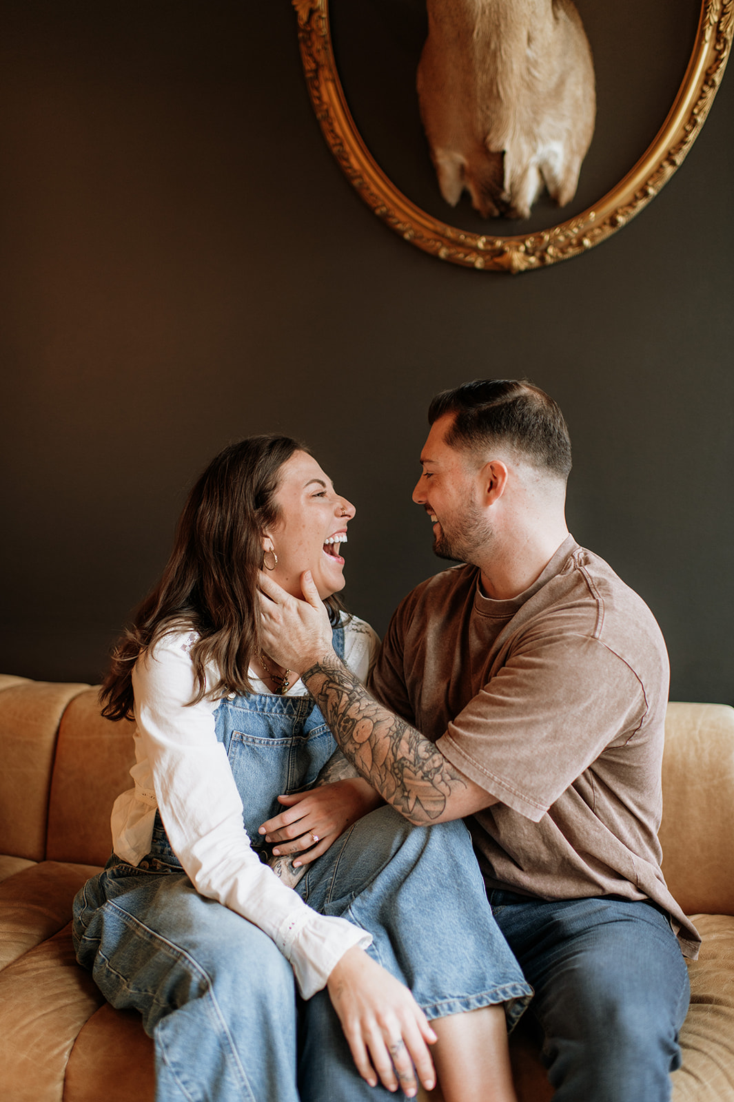 Couple laughing together on couch in antique shop engagement session.