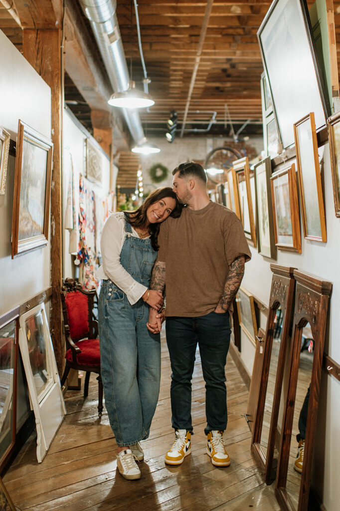 Couple posing in an antique shop holding hands during vintage style engagement photos.