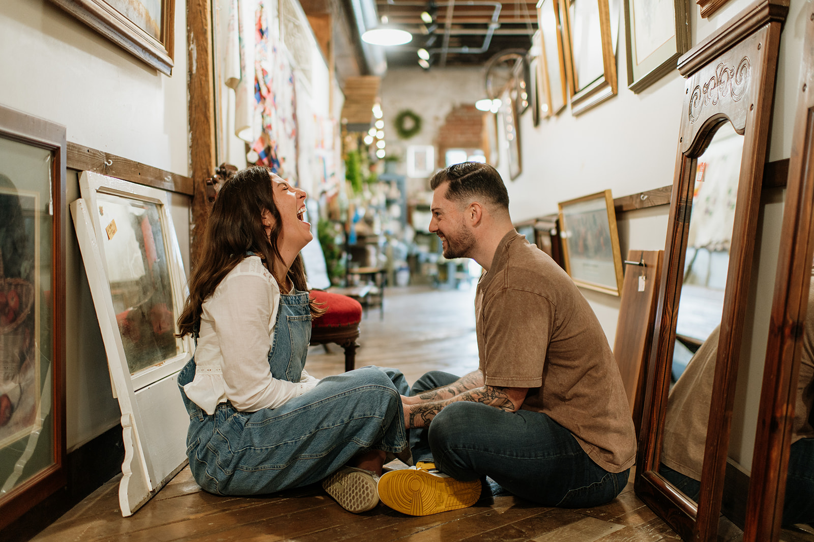 Couple laughing while sitting on wooden floor surrounded by framed artwork.