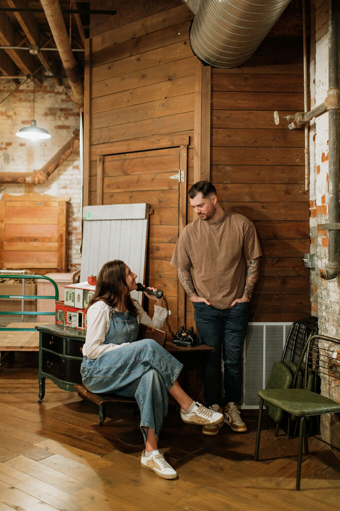Bride-to-be sitting and smiling while holding vintage phone during antique shop engagement photos.