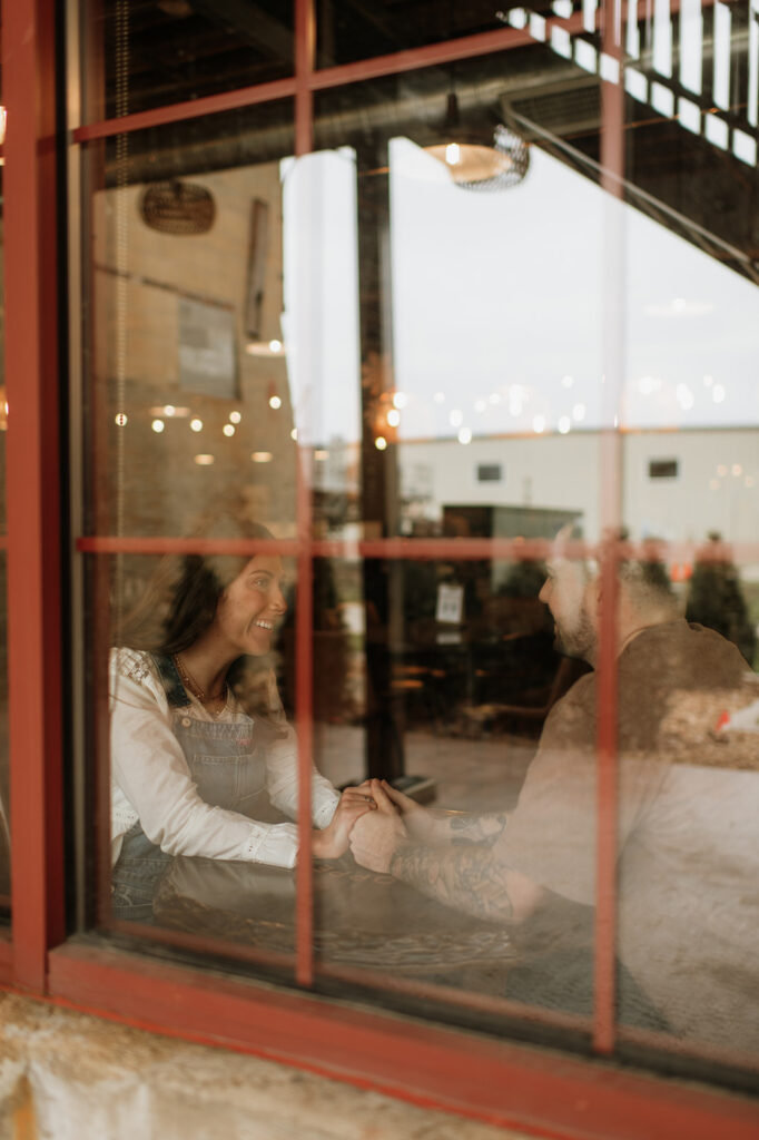 Candid moment of couple holding hands through window.