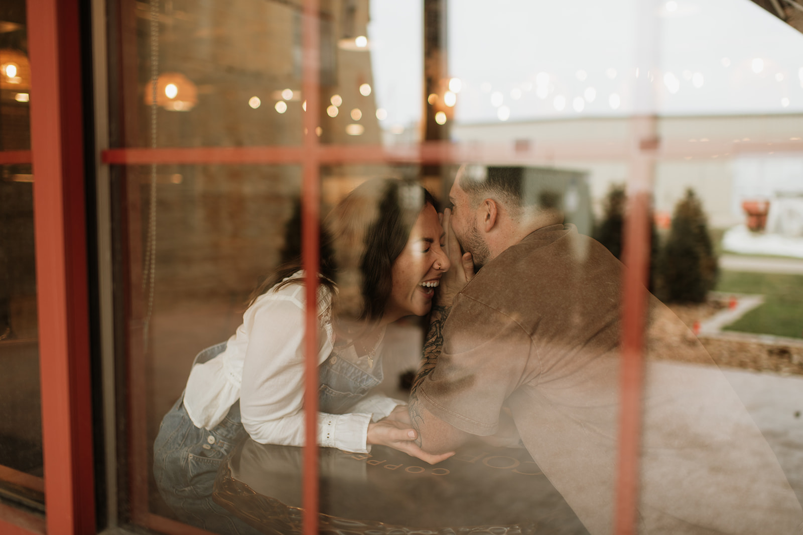 Candid moment of couple laughing together through window during vintage inspired engagement photos.