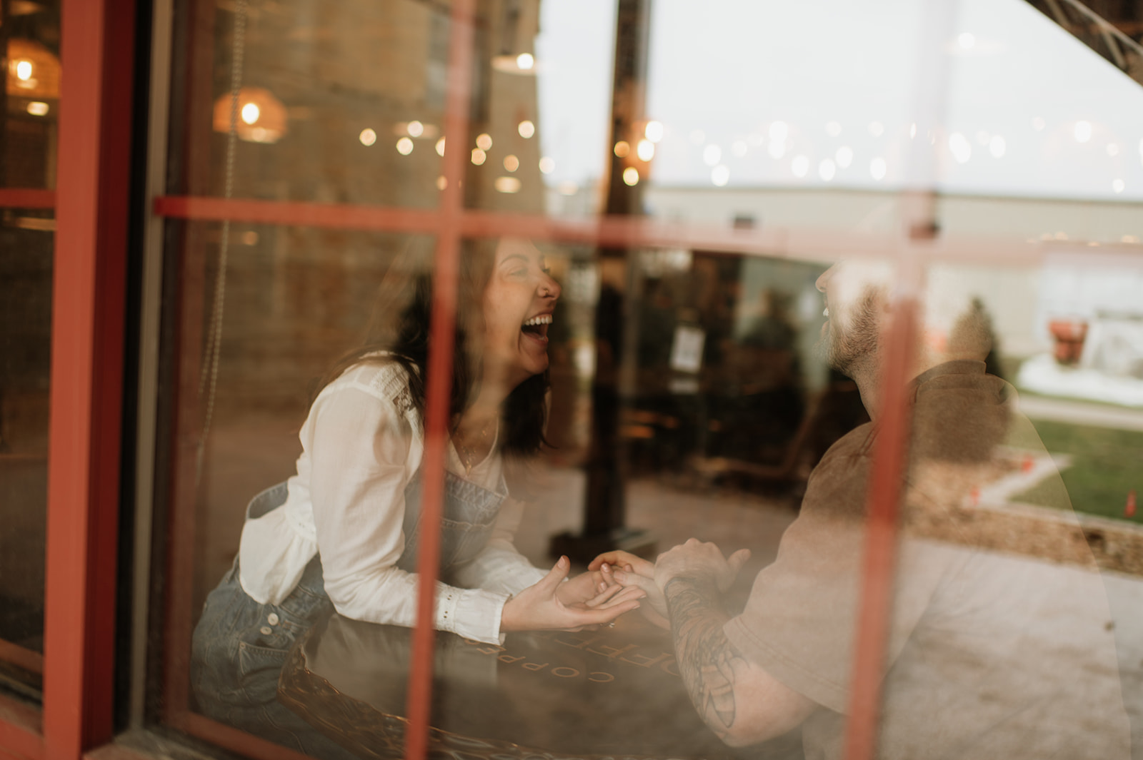Candid moment of couple laughing together through window during vintage inspired engagement photos.