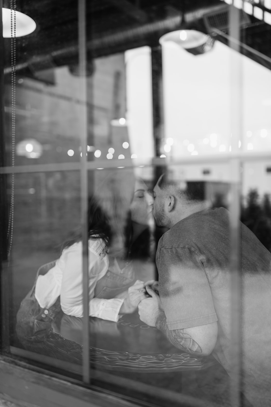 Black and white reflection of couple kissing through window during engagement session.