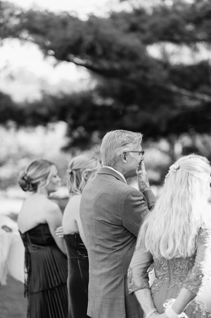 Black and white candid photo of family members watching the bride and groom exchange private vows.