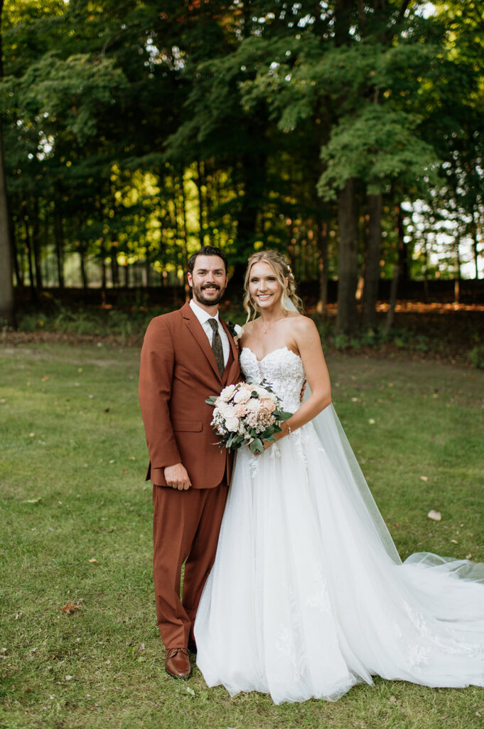 Bride and groom standing together in front of wooded trees during outdoor wedding portraits.