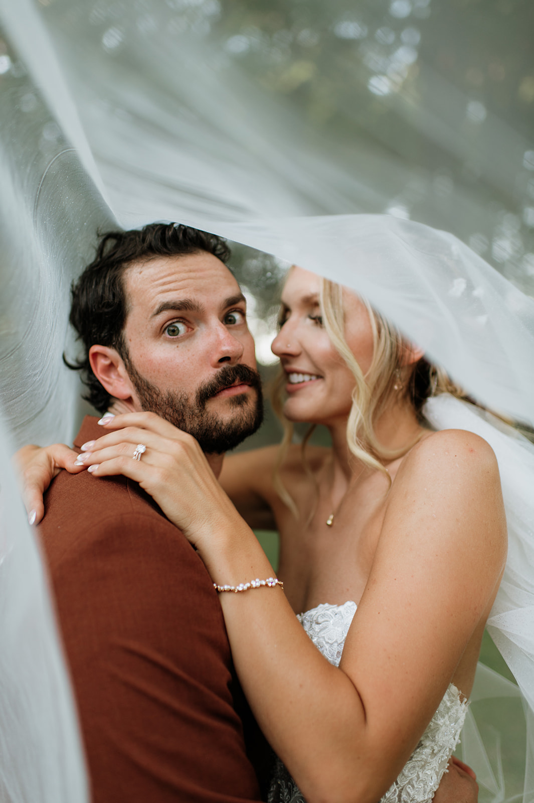 Close up portrait of bride and groom smiling together under veil.