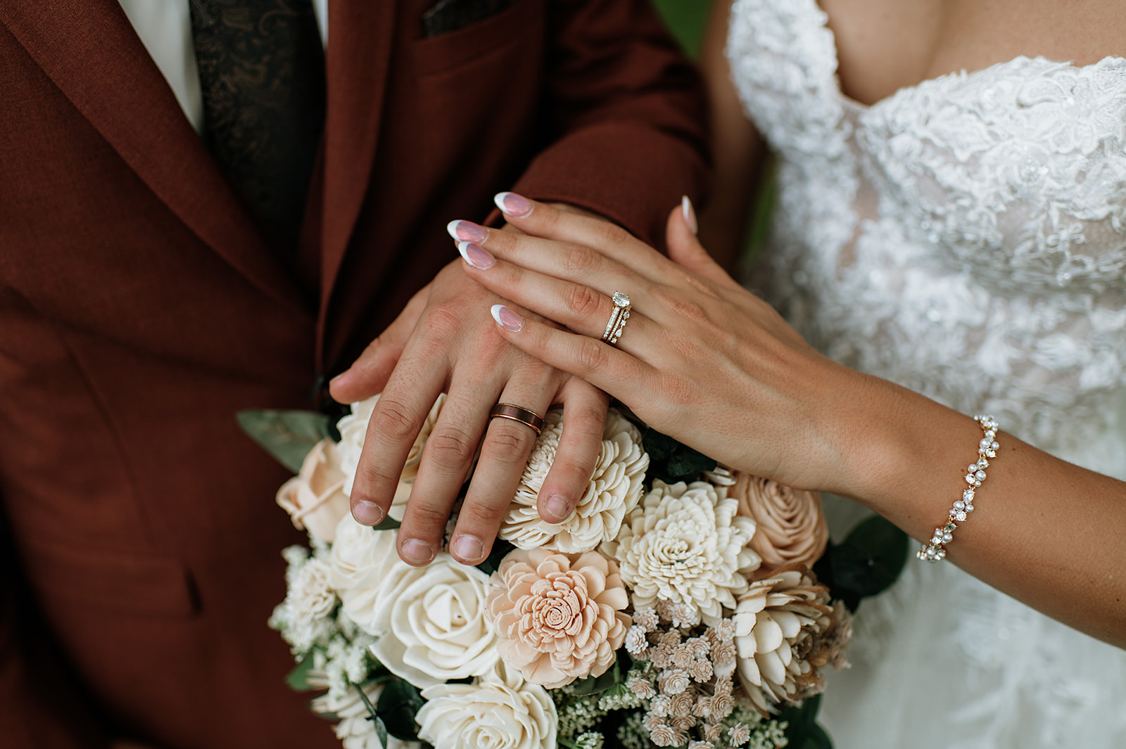 Close up of bride’s engagement ring and wedding band resting on bouquet with groom’s hand.