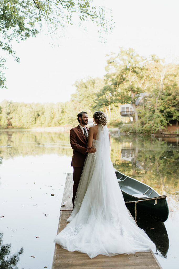Bride and groom standing on dock by lake with canoe during wedding portraits at The Lodge at Rush Lakes.
