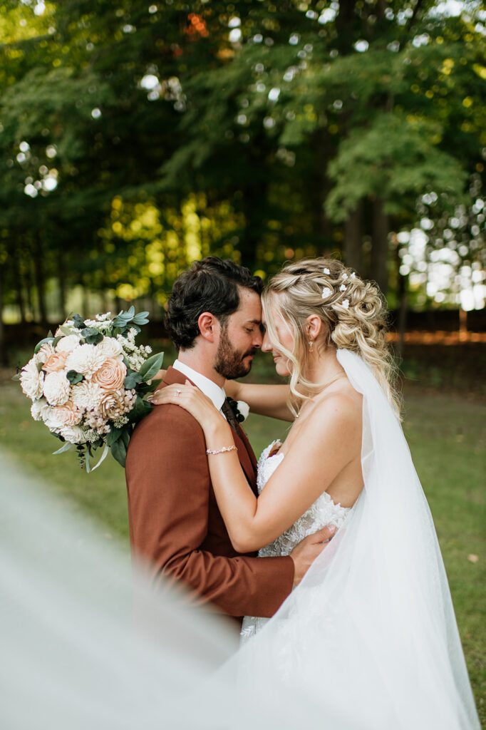 Bride and groom standing together in front of wooded trees during outdoor wedding portraits.