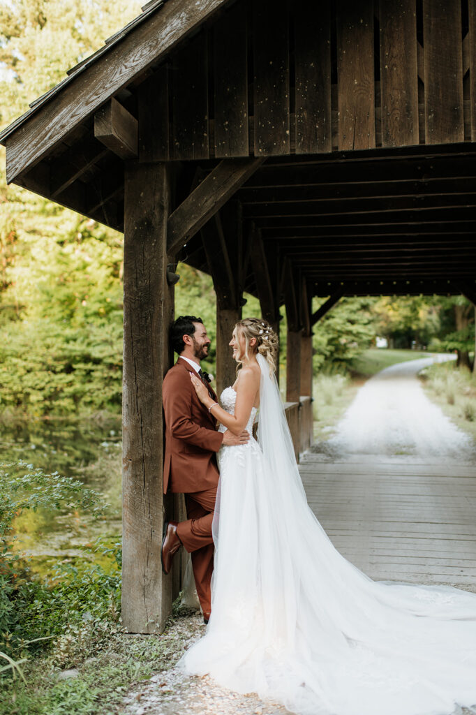 Bride and groom embracing on a wooden covered bridge path during outdoor wedding portraits.