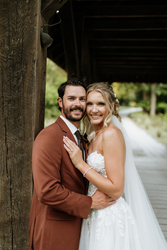 Bride and groom embracing on a wooden covered bridge path during outdoor wedding portraits.