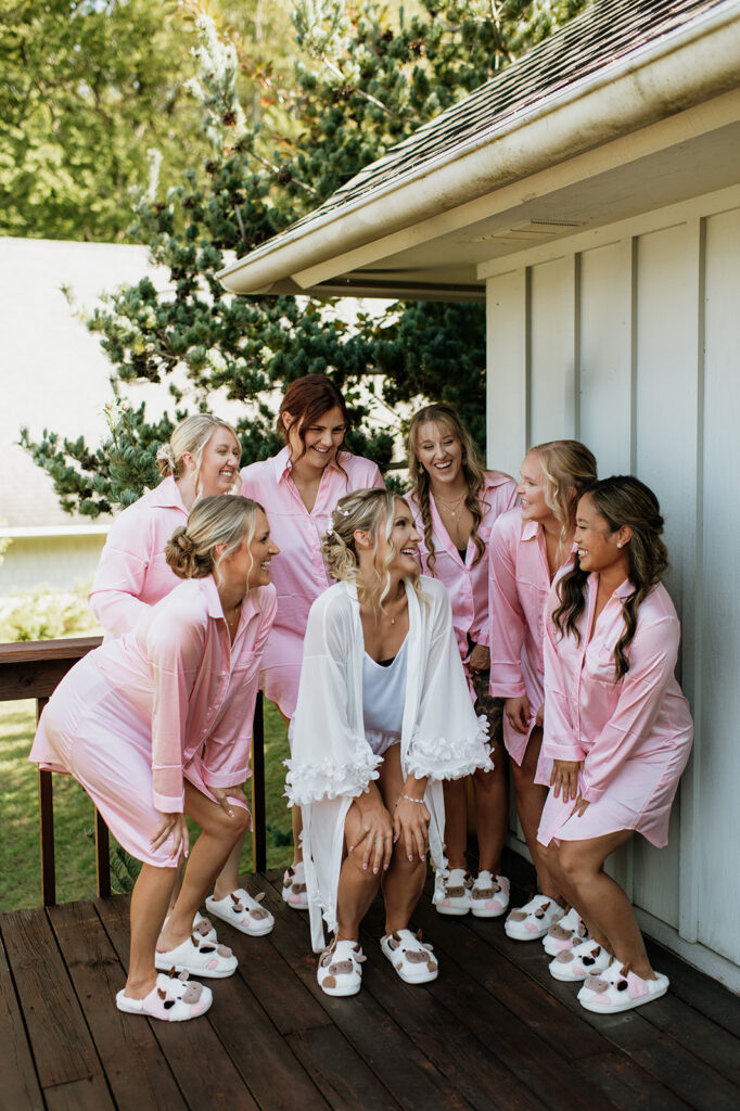 Bride laughing with bridesmaids in pink pajamas while getting ready at The Lodge at Rush Lakes wedding venue in La Porte Indiana.