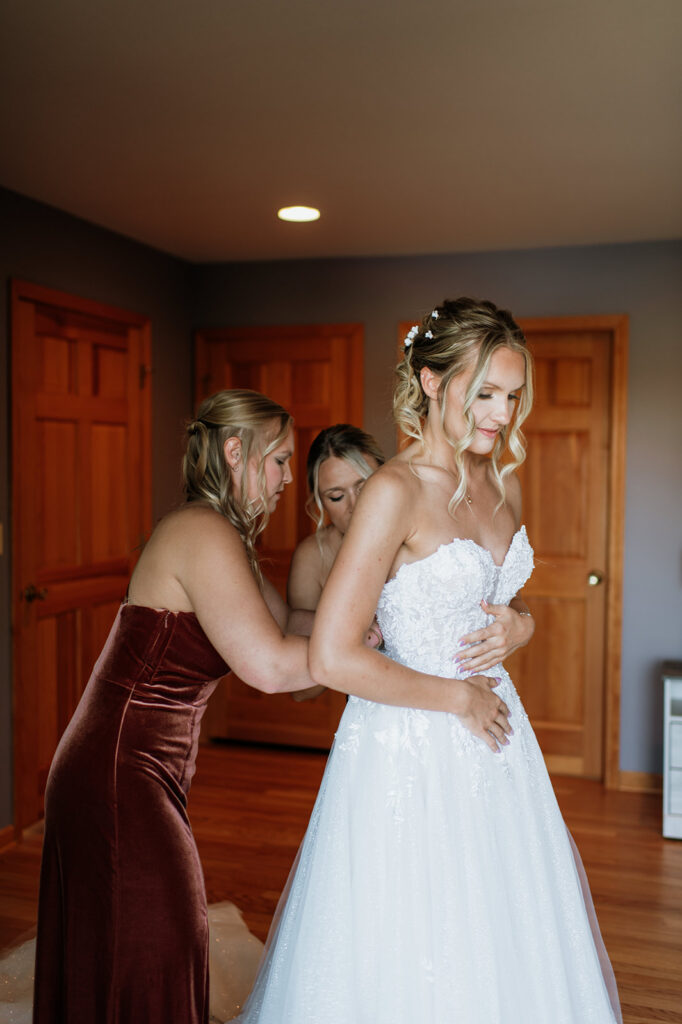 Bride getting into her wedding dress with bridesmaids helping inside the main house at The Lodge at Rush Lakes wedding venue.