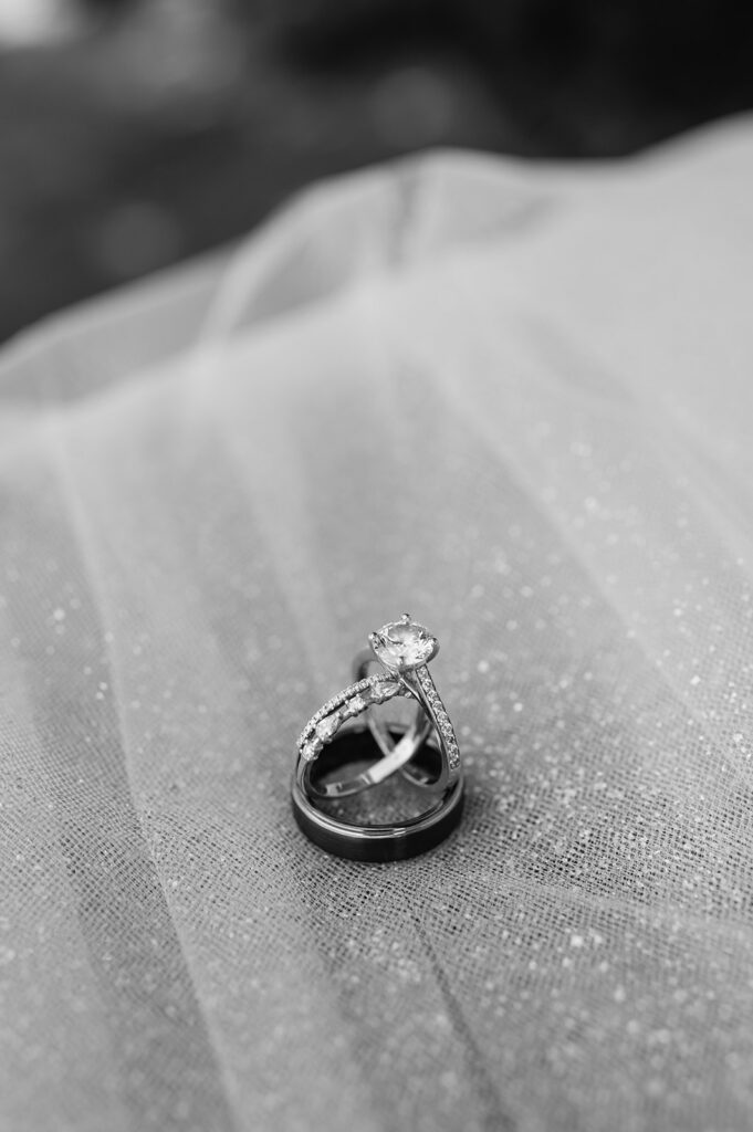 Black and white photo of the brides rings and grooms wedding band styled on the brides veil. 