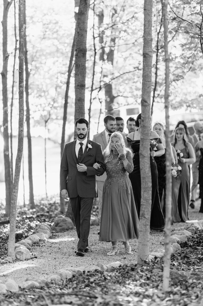 Black and white photo of the groom walking with his mother.
