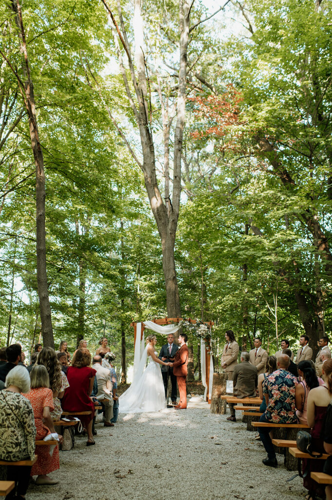 Wide view of outdoor wedding ceremony in the woods at The Lodge at Rush Lakes wedding venue.