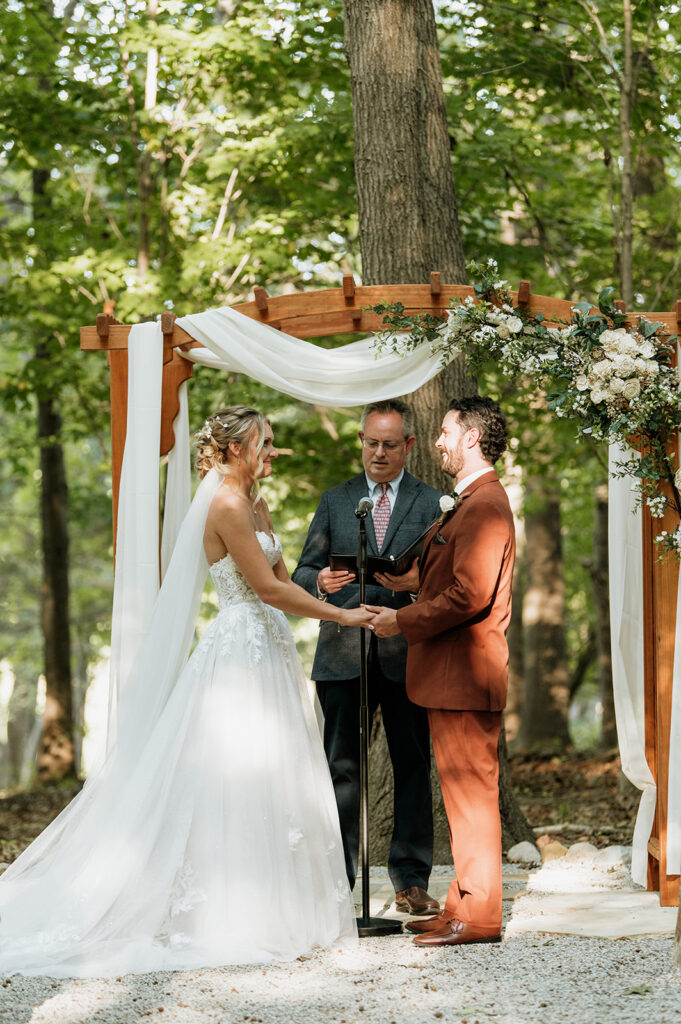 Bride and groom exchanging vows beneath wooden arbor at The Lodge at Rush Lakes wedding.