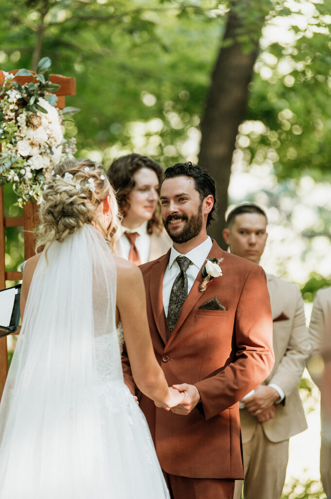 Bride and groom holding hands during ceremony under arbor at The Lodge at Rush Lakes wedding venue.