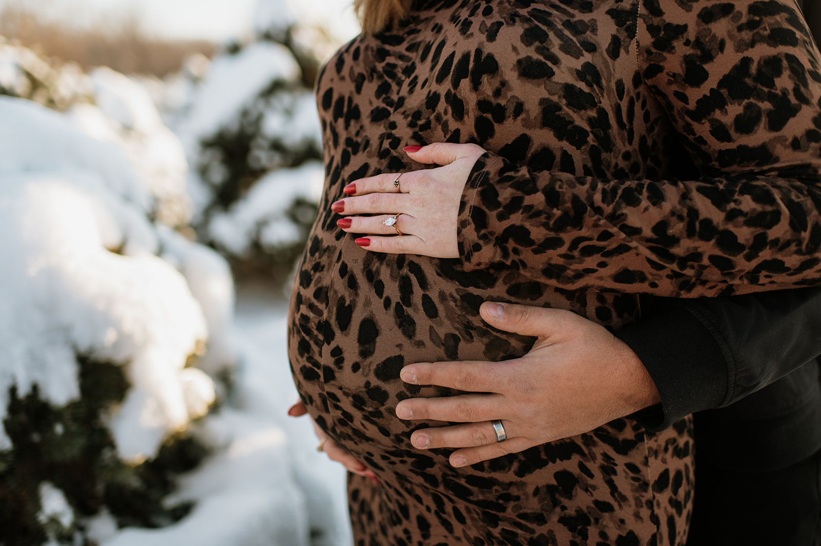 Close-up maternity photo of hands holding baby bump during outdoor winter maternity photos.