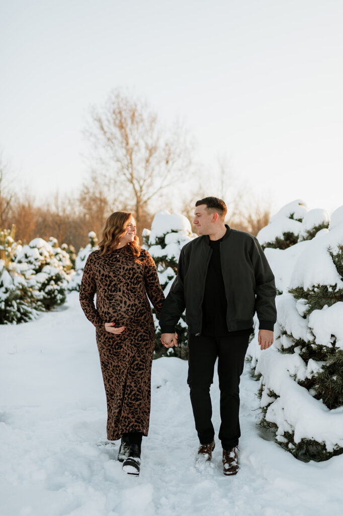 Couple walking in a snowy evergreen tree farm in Northern Indiana.