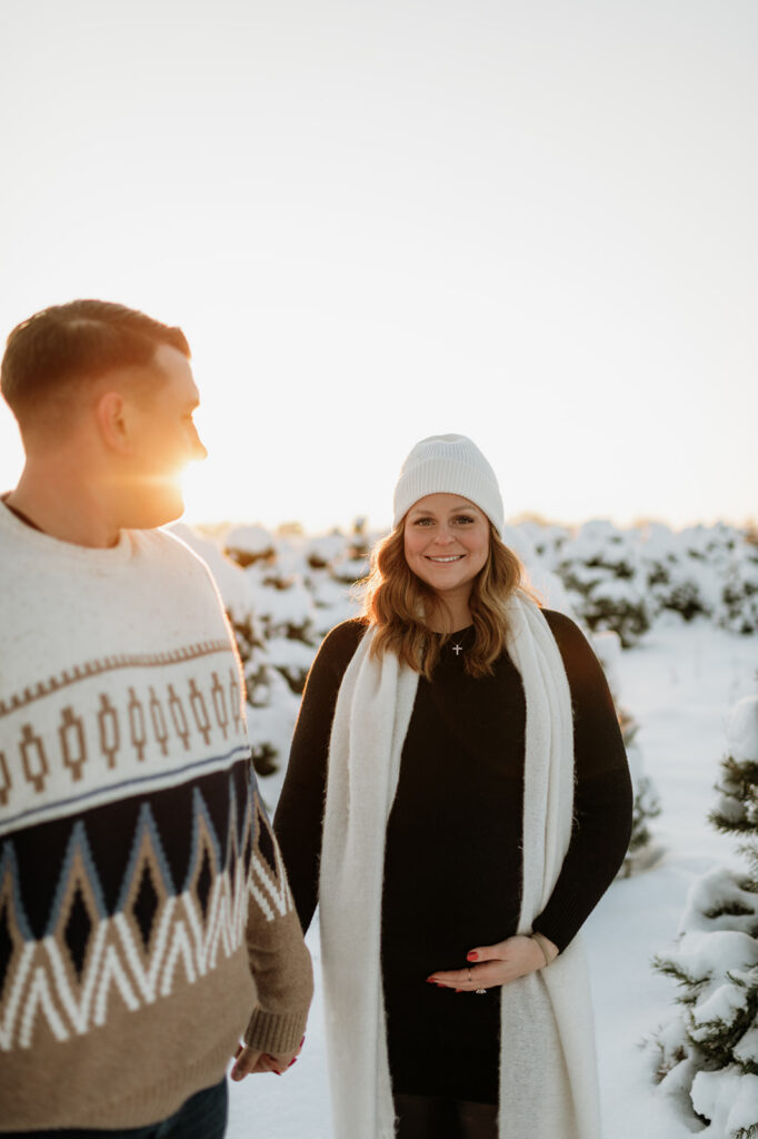 Couple walking through the snow during outdoor winter maternity photos at Flickinger Farms tree farm in Elkhart, Indiana.