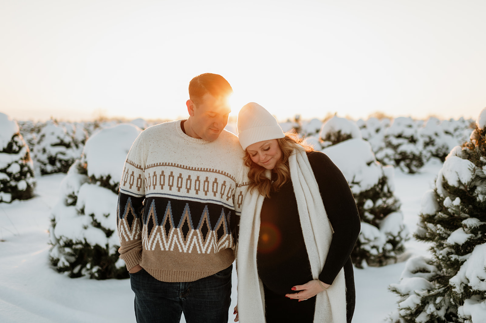 Expectant couple sharing a quiet moment among snow-covered pine trees during tree farm maternity photos at Flickinger Farms.