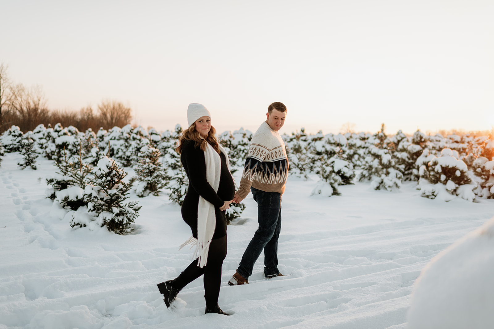 Expectant couple walking through a snowy tree farm in Northern Indiana.