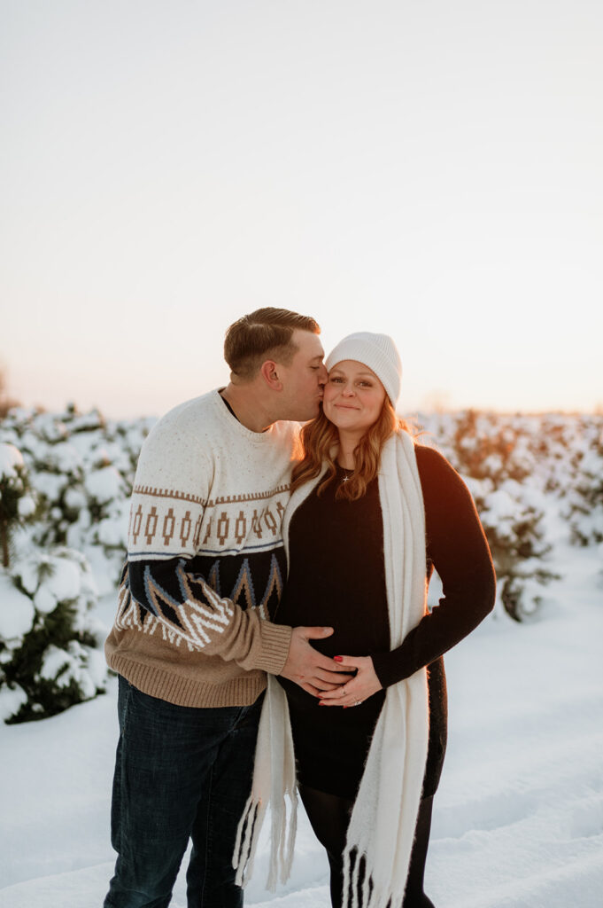Man kissing his pregnant partner during their outdoor winter maternity photos in Northern Indiana.
