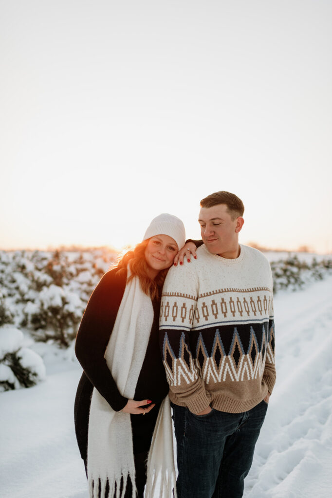Woman leaning on her partner during their outdoor winter maternity photos at sunset.