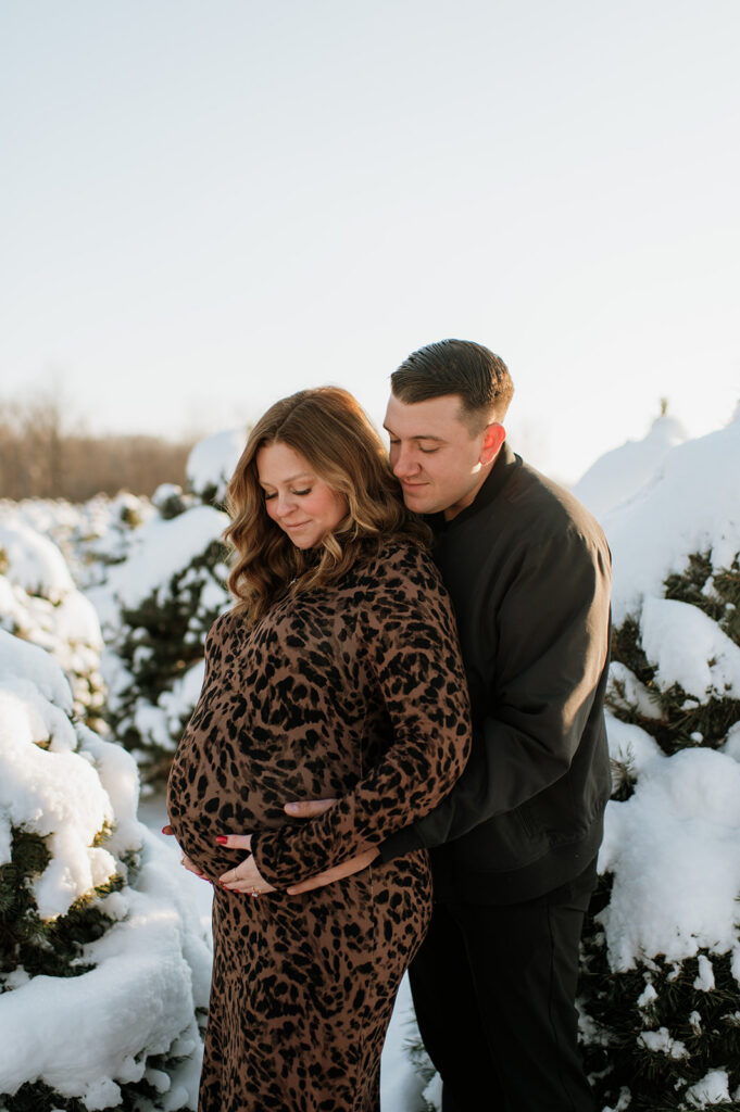 Couple posing at a tree farm for their outdoor winter maternity photos in Northern Indiana.