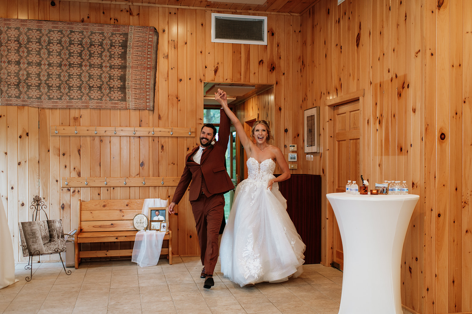 Bride and groom entering their wedding reception together with hands raised in celebration inside the reception pavilion.