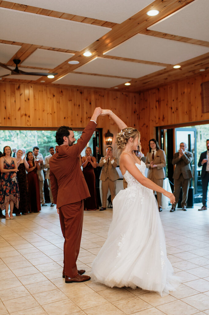 Bride and groom sharing their first dance surrounded by guests inside a wood-paneled reception pavilion.