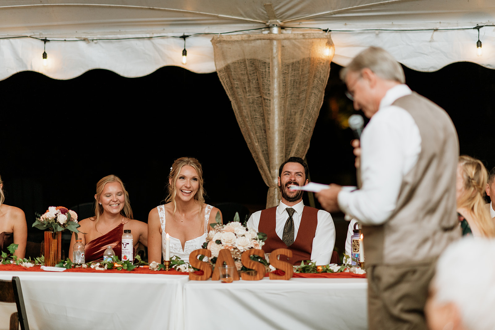 Bride and groom laughing during heartfelt wedding speech at their reception table.