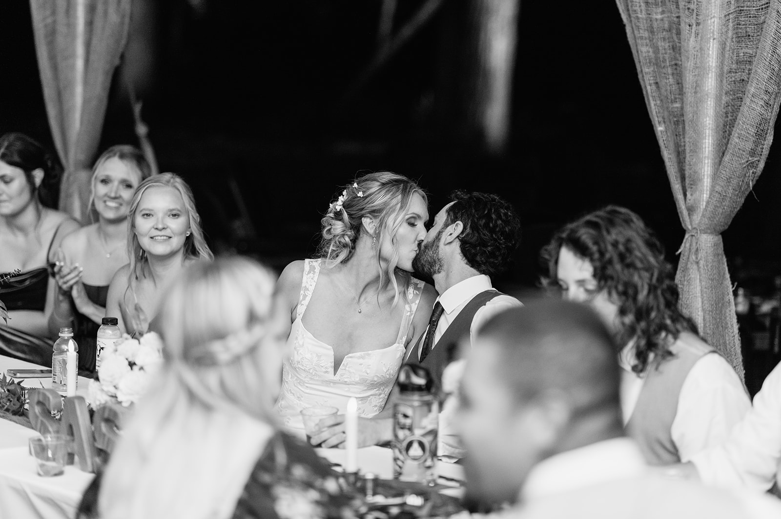Black and white photo of a bride and groom kissing during their reception.