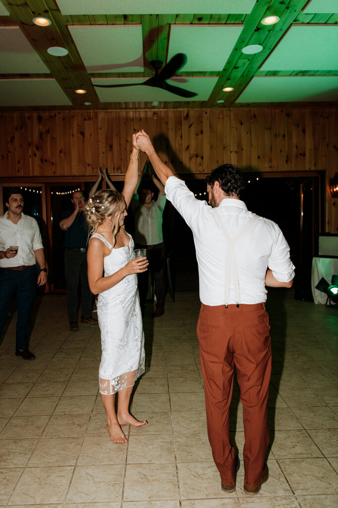 Bride and groom twirling on the dance floor during reception party with guests cheering.