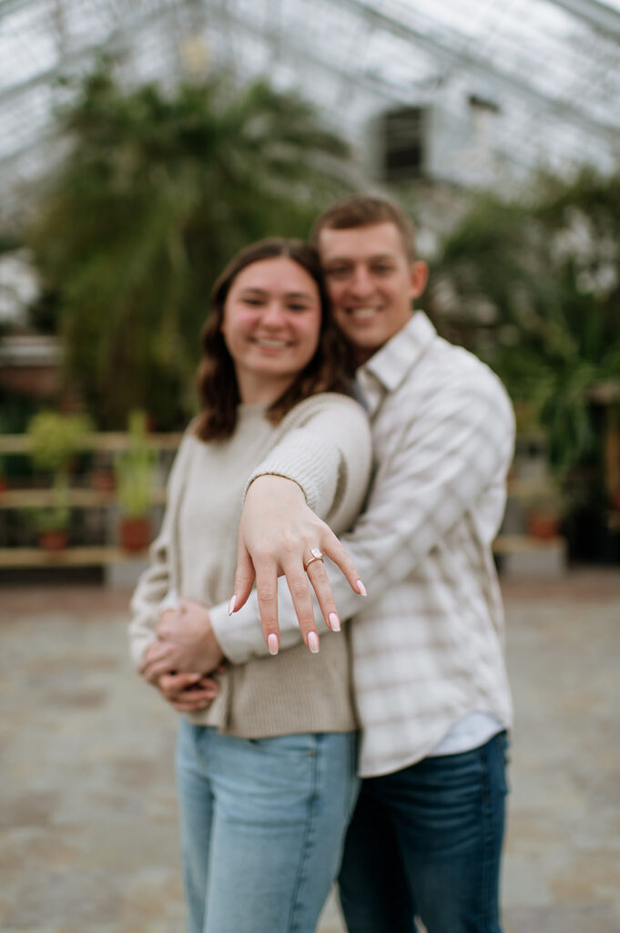 Engagement ring focus shot after South Bend Indiana surprise proposal with couple in background.