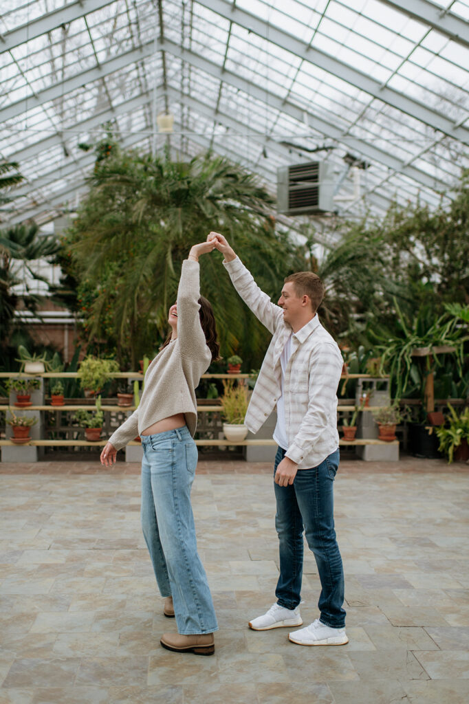 Playful twirl moment after South Bend Indiana surprise proposal inside greenhouse setting.