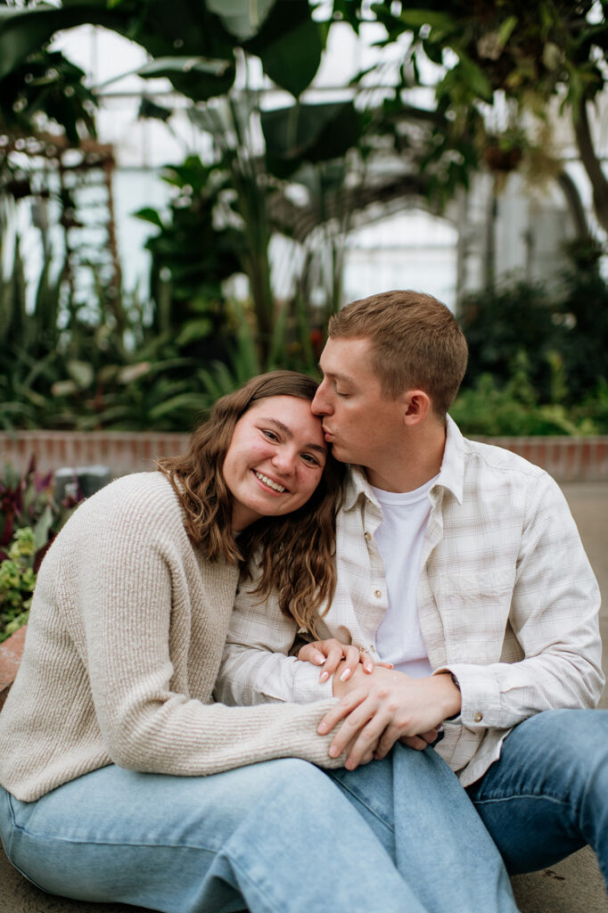 Man kissing his fiancés forehead during their surprise proposal photoshoot in South Bend, Indiana at Potawatomi Conservatories.