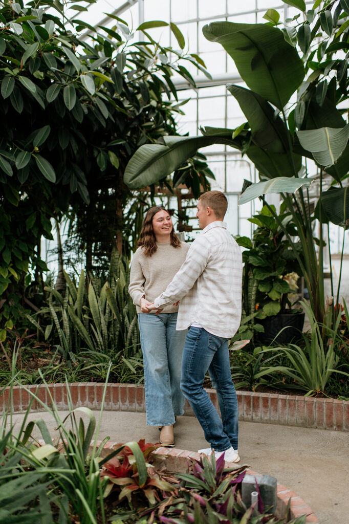 Couple holding hands and posing inside of Potawatomi Conservatories after their surprise proposal.
