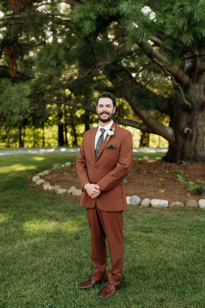 Groom portrait in rust colored suit outdoors at The Lodge at Rush Lakes wedding venue in La Porte Indiana.