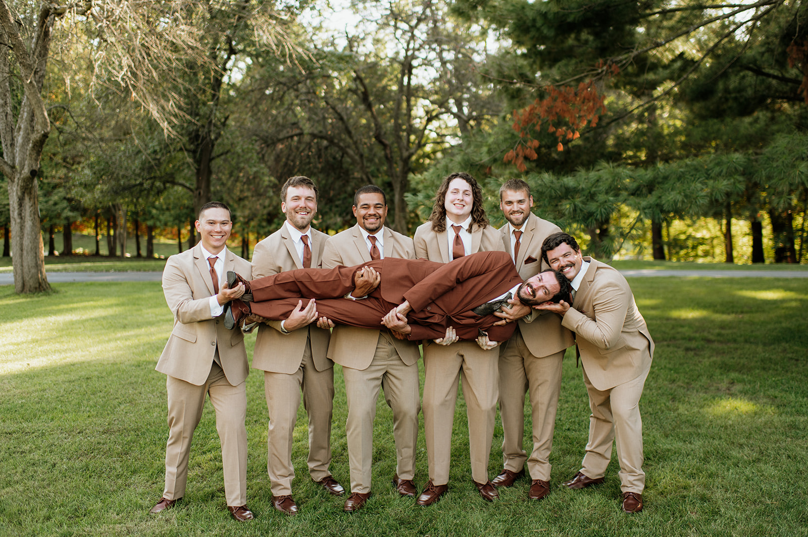 Groomsmen holding groom and laughing during fun wedding party photo at The Lodge at Rush Lakes wedding venue.