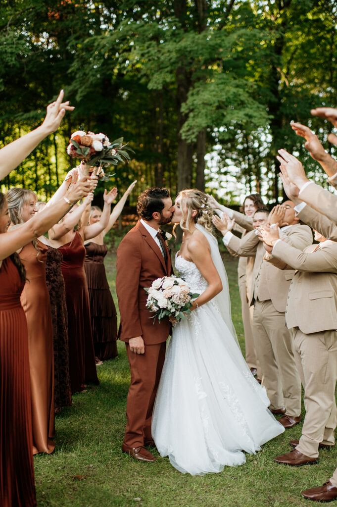 Bride and groom kissing surrounded by cheering wedding party at The Lodge at Rush Lakes wedding.