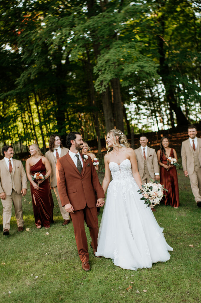 Bride and groom walking with wedding party through wooded grounds at The Lodge at Rush Lakes..